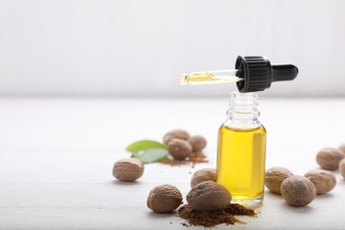 Photo of Bottle of nutmeg oil, pipette, nuts and powder on white wooden table, space for text