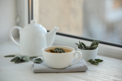 Photo of Sage tea and green leaves on white wooden windowsill