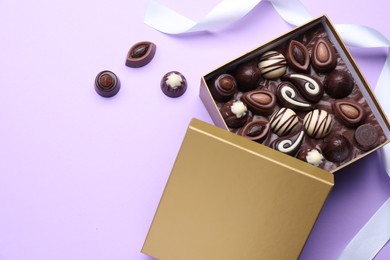 Photo of Open box of delicious chocolate candies on violet background, flat lay. Space for text