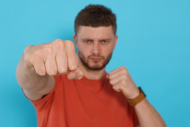 Young man ready to fight against light blue background, focus on hand. Space for text