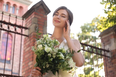 Gorgeous bride in beautiful wedding dress with bouquet near church