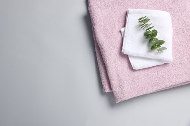 Soft folded towels with eucalyptus branch on light grey background, top view. Space for text