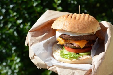 Delicious burger in paper wrap outdoors, closeup