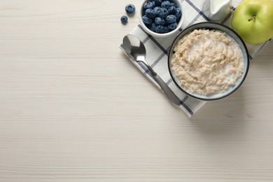 Tasty oatmeal porridge served on light wooden table, flat lay. Space for text