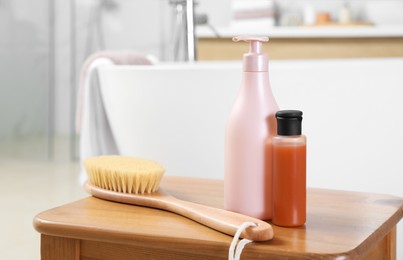 Bottles of shower gels and brush on wooden table near tub in bathroom, space for text