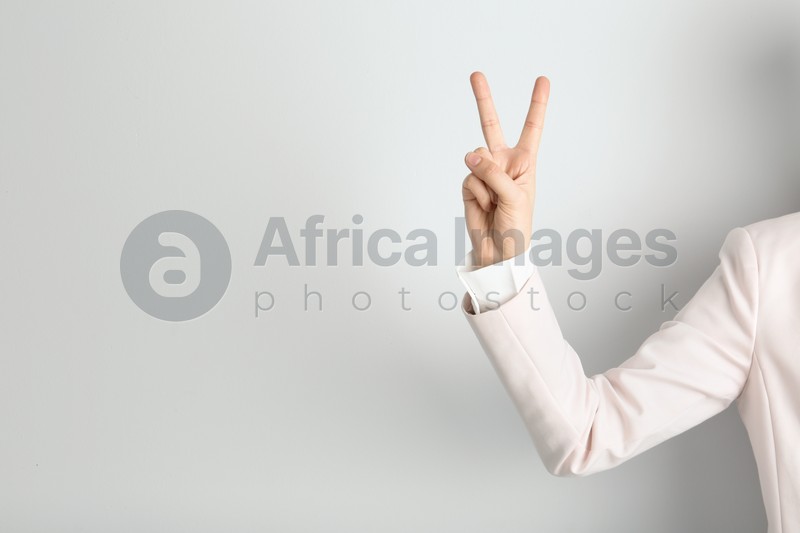 Photo of Young woman showing victory gesture on light background. Space for text