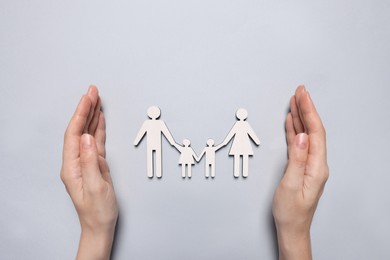Woman protecting figures of family on light background, top view. Insurance concept