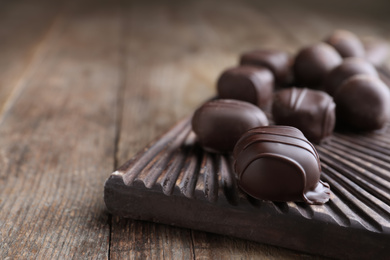 Tasty dark chocolate candies on wooden board, closeup