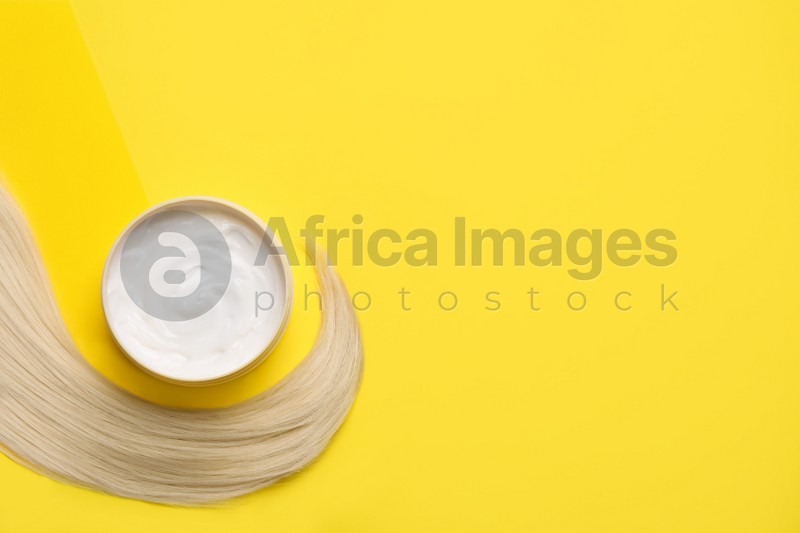 Lock of healthy blond hair and cosmetic product on yellow background, flat lay. Space for text