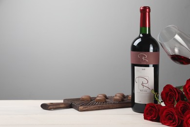 Bottle of red wine, beautiful roses and chocolate candies on white wooden table. Space for text