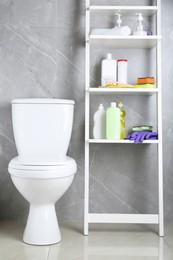 Photo of Toilet bowl and shelving unit with cleaning supplies indoors
