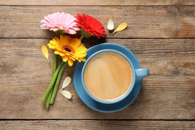 Photo of Beautiful colorful gerbera flowers, petals and cup of coffee on wooden table, flat lay