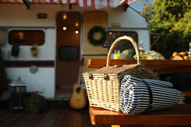 Wicker basket with picnic blanket on wooden bench near motorhome. Camping season