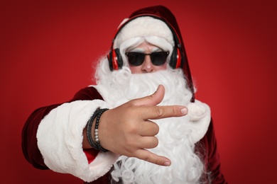 Photo of Santa Claus with headphones listening to Christmas music on red background, focus on hand