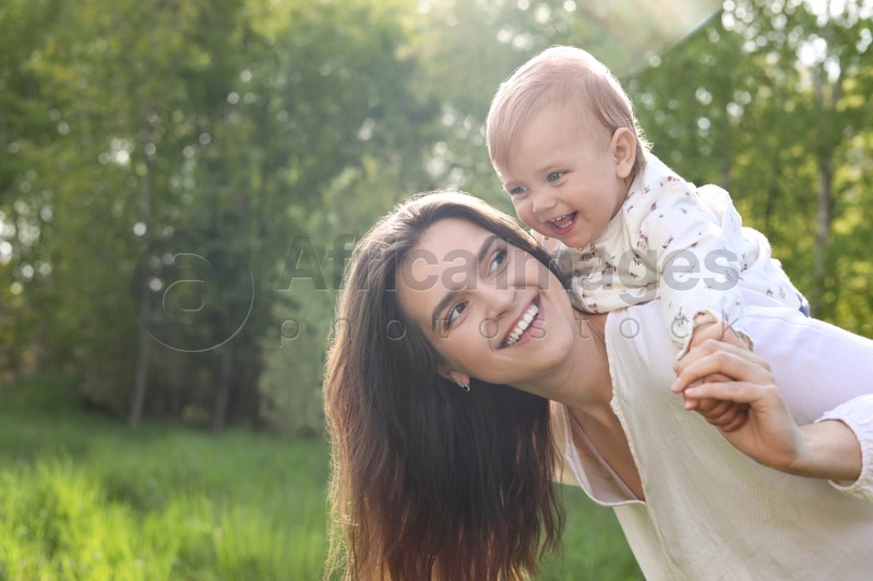 Happy mother playing with her cute baby in park on sunny day, space for text