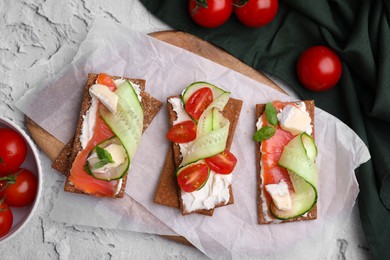 Tasty rye crispbreads with salmon, cream cheese and vegetables on grey textured table, flat lay