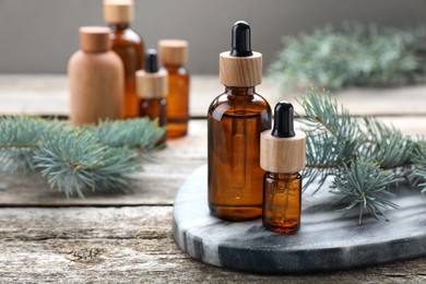 Bottles of spruce essential oil and fresh twigs on wooden table, space for text