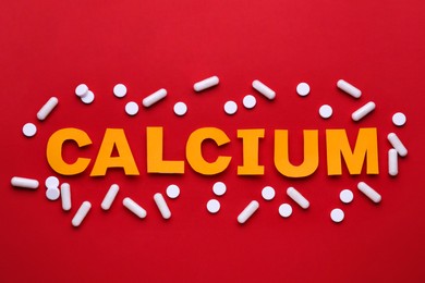 Word Calcium made of orange letters and white pills on red background, flat lay