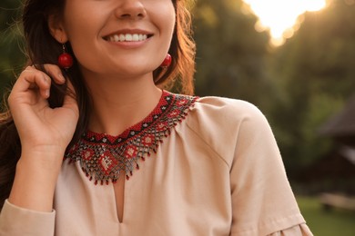 Woman wearing beautiful ornate beaded necklace and red earrings in countryside, closeup. Ukrainian national jewelry