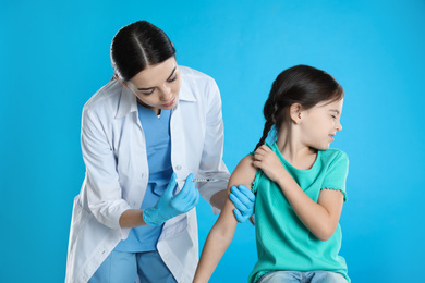 Doctor vaccinating little child on light blue background