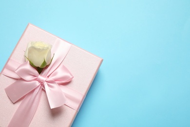 Pink gift box with flower on light blue background, top view. Space for text