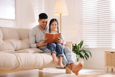 Father and daughter reading book on sofa at home