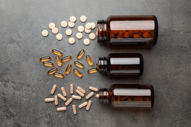 Photo of Overturned bottles with different dietary supplements on grey table, flat lay