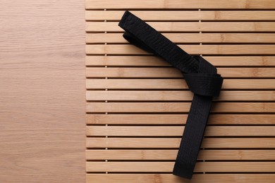 Tied black belt on wooden background, top view with space for text. Oriental martial arts