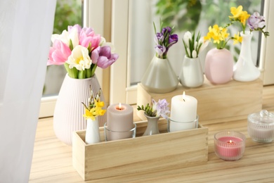 Photo of Beautiful spring flowers with burning candles on window sill