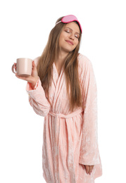 Young woman in bathrobe with sleep mask and cup of beverage on white background