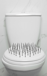 Toilet bowl with nails near marble wall. Hemorrhoids concept
