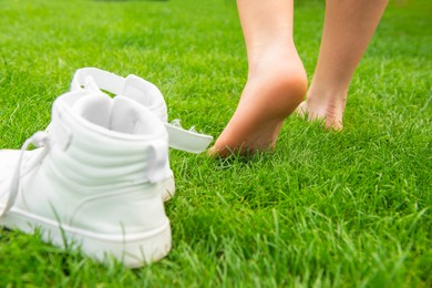 Woman leaving her sneakers and walking away barefoot on green grass, closeup