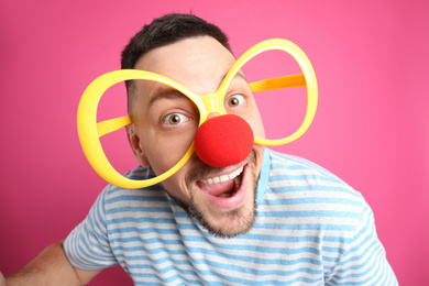 Photo of Joyful man with large glasses and clown nose on pink background. April fool's day