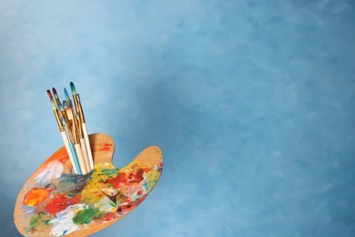Photo of Many paintbrushes and palette on light blue background, space for text