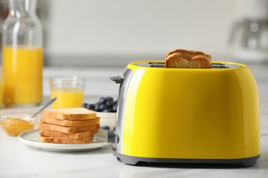 Yellow toaster with roasted bread slices, jam, juice and blueberries on white marble table