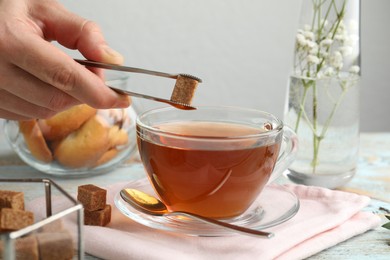 Photo of Woman adding brown sugar cube to aromatic tea at wooden table, closeup