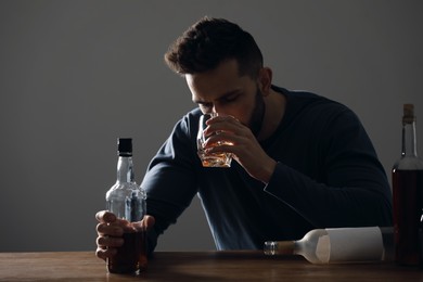 Addicted man drinking alcohol at wooden table indoors