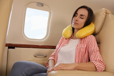Young woman with travel pillow sleeping in airplane during flight
