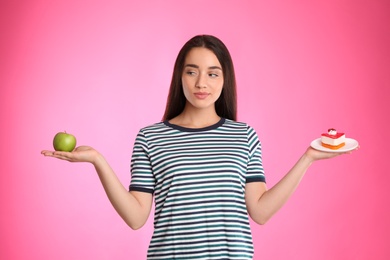 Concept of choice. Woman holding apple and cake on pink background