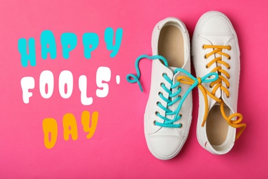 Shoes tied together on pink background, flat lay. Happy Fool's Day
