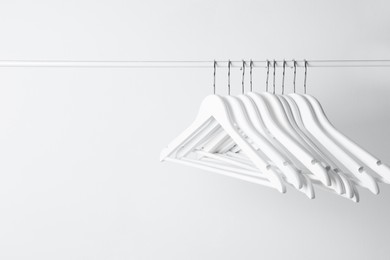 Photo of White clothes hangers on metal rail against light background. Space for text