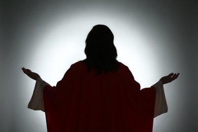 Silhouette of Jesus Christ with outstretched arms on color background, back view