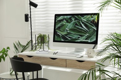 Photo of Comfortable workplace with modern computer and green plants in room. Interior design