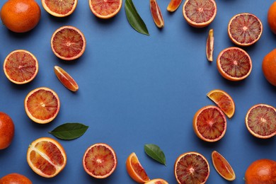 Frame of ripe sicilian oranges and leaves on blue background, flat lay. Space for text