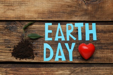 Words Earth Day, soil with plant and decorative heart on wooden table, flat lay