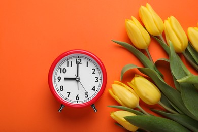 Photo of Red alarm clock and beautiful tulips on orange background, flat lay. Spring time