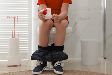 Boy holding toilet paper with blood stain in rest room, closeup. Hemorrhoid concept