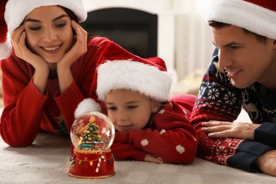 Family in Santa hats playing with snow globe while lying on floor
