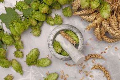 Mortar with pestle, fresh hops and ears of wheat on light grey marble table, flat lay