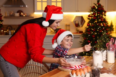 Photo of Happy mother and her son making dough for Christmas cookies at home